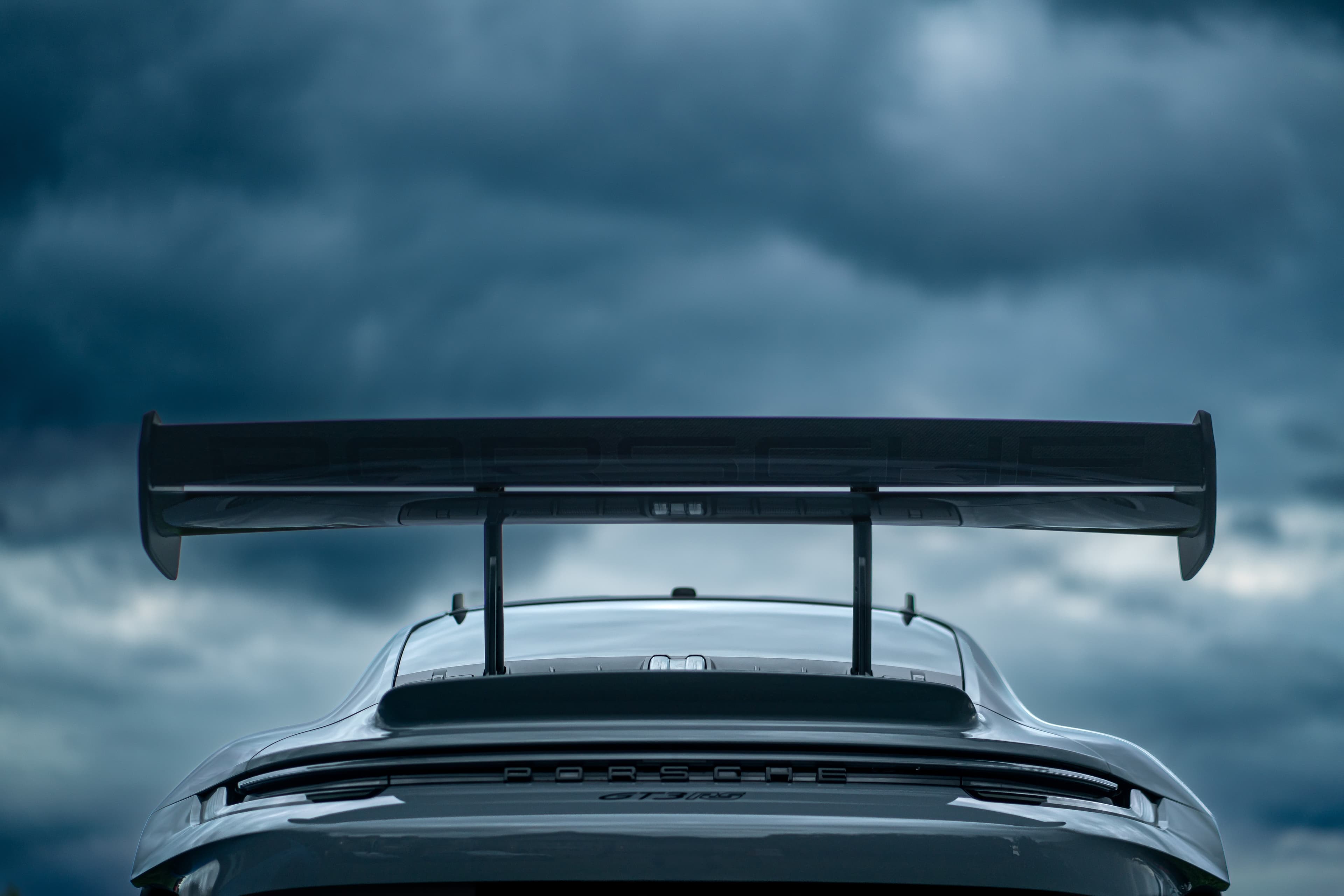 Rear wing of a silver Porsche 911 GT3 RS against storm clouds