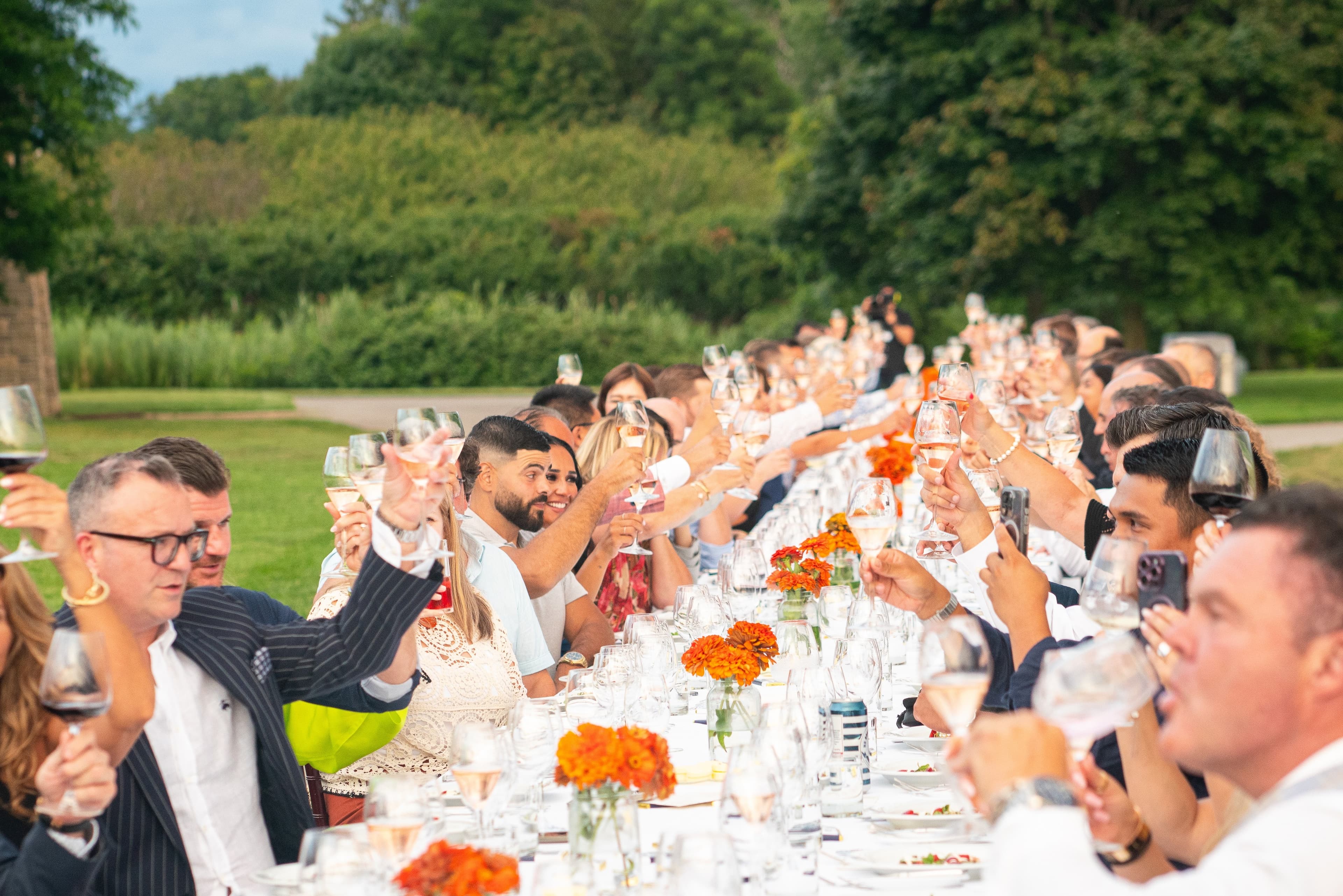 Guests raise rosé glasses in a toast at a long outdoor winery dinner table
