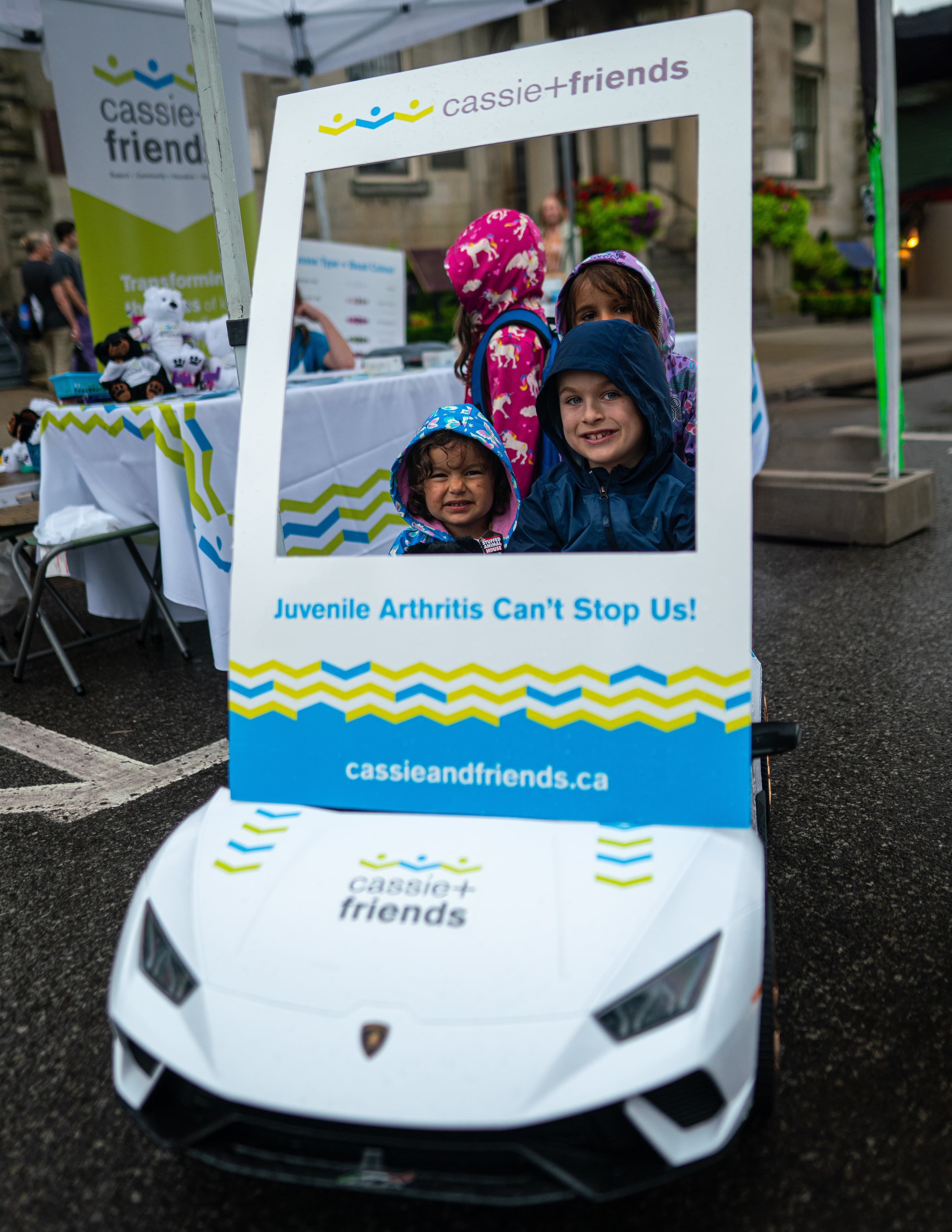 Children pose in a Cassie+Friends photo frame on a ride-on Lamborghini