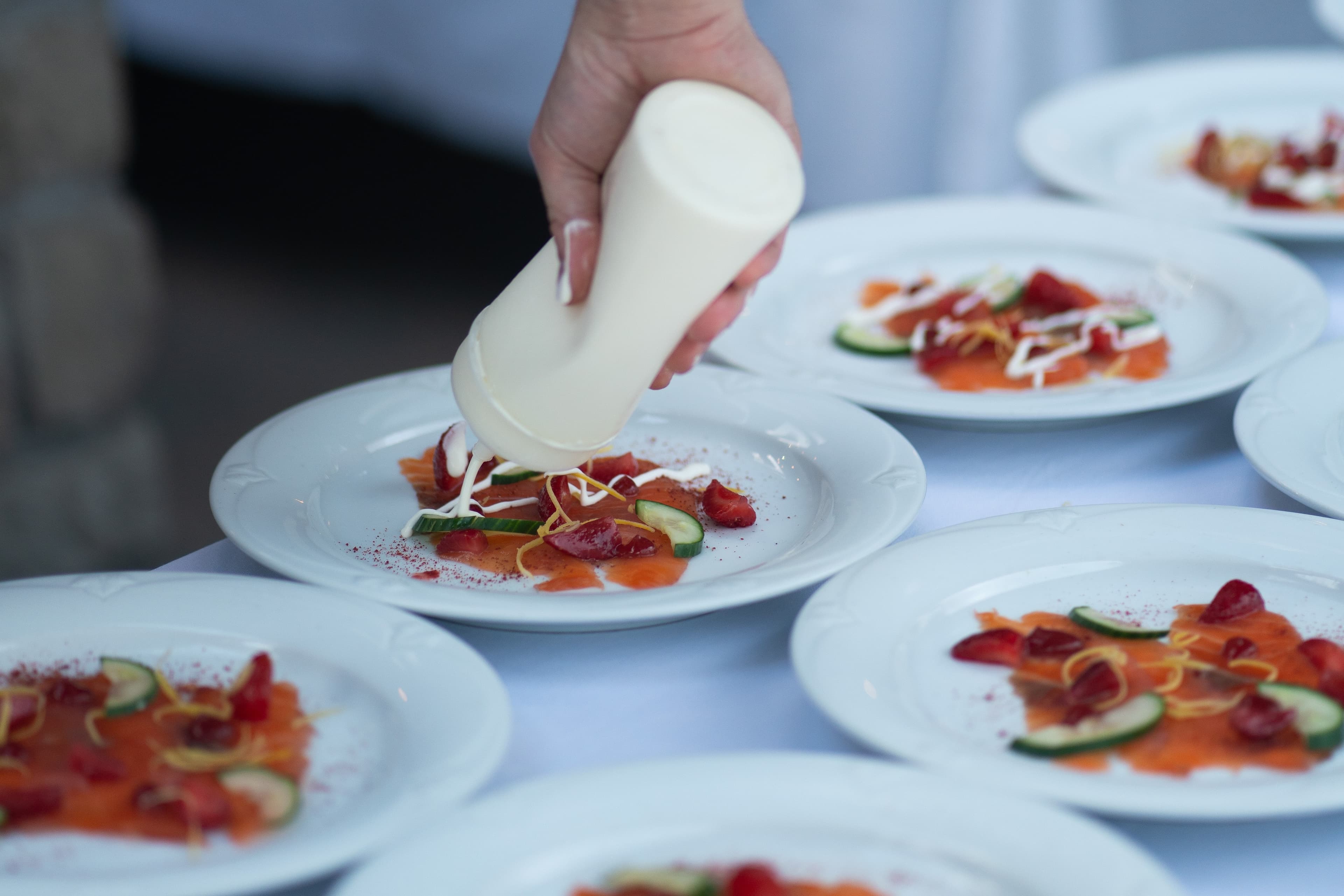 Hand drizzling sauce over plated smoked salmon at a dinner
