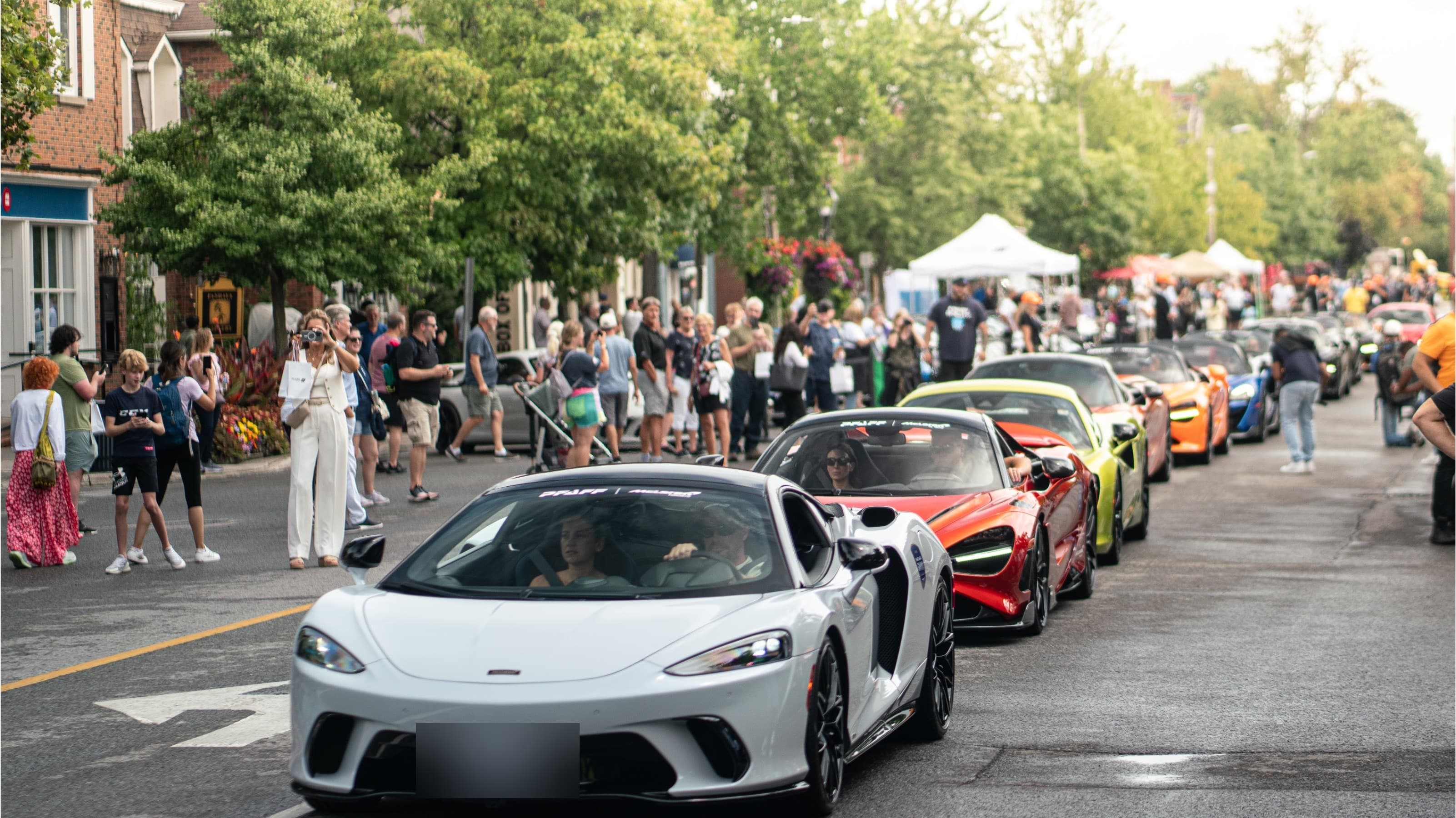 White McLaren GT leads a supercar parade past sidewalk crowds